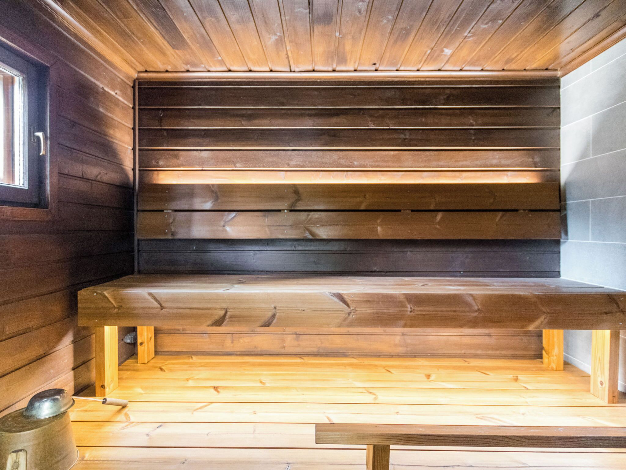 A wooden bench with a slatted design, a metal pot, and a wooden floor.