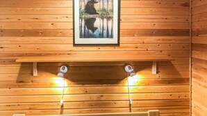 A wooden cabin room with a bed, two wall-mounted lights, and a framed picture of a bear. - Pikku-metso by Interhome (Kuusamo)