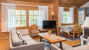 A cozy cabin-style room with a sofa, chairs, a dining table, a TV, and a fireplace.