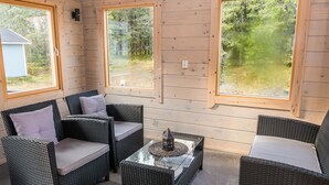 A wooden-paneled room with wicker furniture, large windows, and a view of a forest.