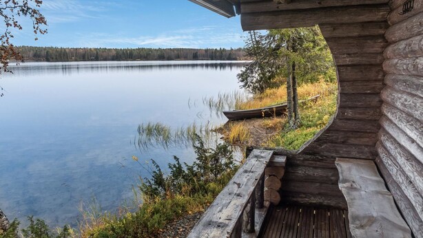 A wooden cabin with a view of a calm lake and a dock.