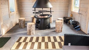 A cozy cabin interior with a wood-burning stove, wooden stools, and a woven rug.