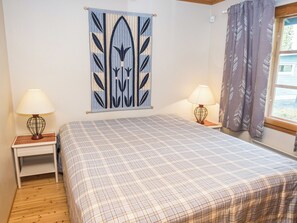 Een slaapkamer met een bed, twee nachtkastjes met lampen, een wanddecoratie en een raam met gordijnen.