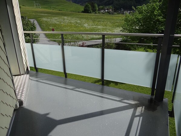 Ein Balkon mit Metallgeländer, der auf eine grüne Landschaft mit einer Straße und Gebäuden blickt.