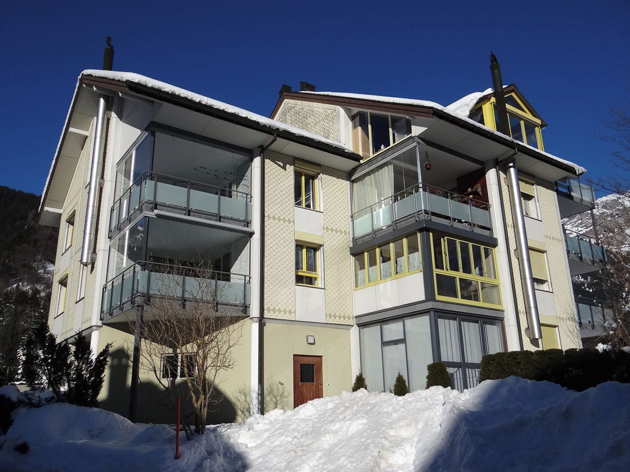 Un edificio de varios pisos con balcones, una puerta visible y nieve en el suelo.