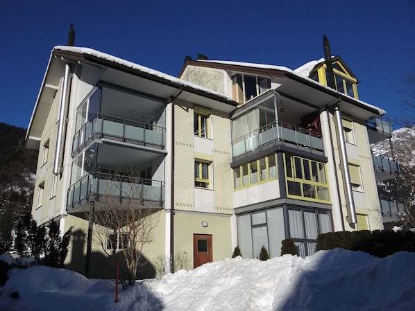 Un immeuble à plusieurs étages, doté de balcons, avec une porte bien visible et de la neige au sol.