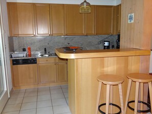 A kitchen with wooden cabinets, a sink, a coffee maker, and two stools.
