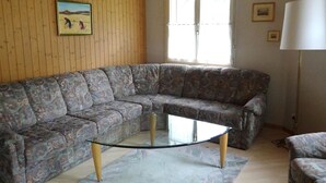 A living room with a sectional sofa, a glass coffee table, and a lamp.