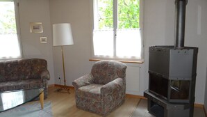 A living room with a sofa, armchair, lamp, and a wood-burning stove.