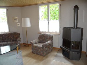 Un salon avec un canapé, un fauteuil, une lampe et un poêle à bois.