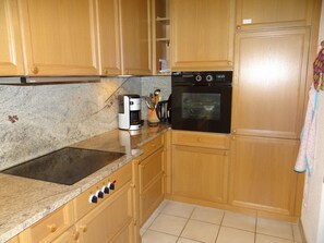 Une cuisine avec des meubles de rangement en bois, un four encastré, une machine à café et une cuisinière.