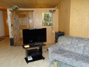 Ein Wohnzimmer mit Flachbildfernseher auf einem Schrank, einem gemusterten Sofa, einem Holzschrank und einem Gemälde an der Wand.
