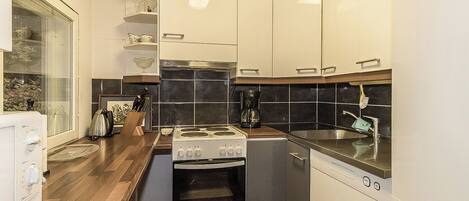 Een compacte keuken met een ingebouwde oven, een koffiezetapparaat en een vaatwasser.
