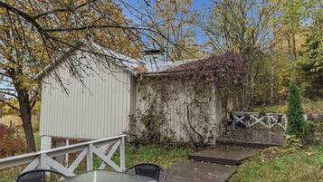 A rustic outdoor seating area with a table and chairs, a wooden deck, and a shed with vines.