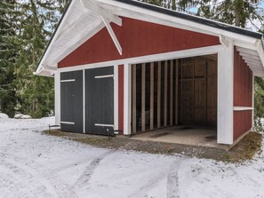 Un bâtiment rouge et blanc avec une porte de garage, entouré de neige et d’arbres.