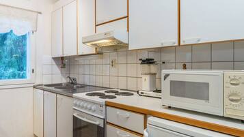 Een keuken met witte kasten, een fornuis, een magnetron en een raam met uitzicht op bomen.