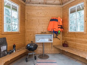 L’intérieur d’une cabane avec un mur en bois, un barbecue, un porte-manteau suspendu et une fenêtre.