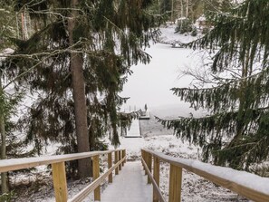 Un escalier en bois mène à une jetée surplombant une étendue d’eau, le tout étant entouré d’arbres couverts de neige.