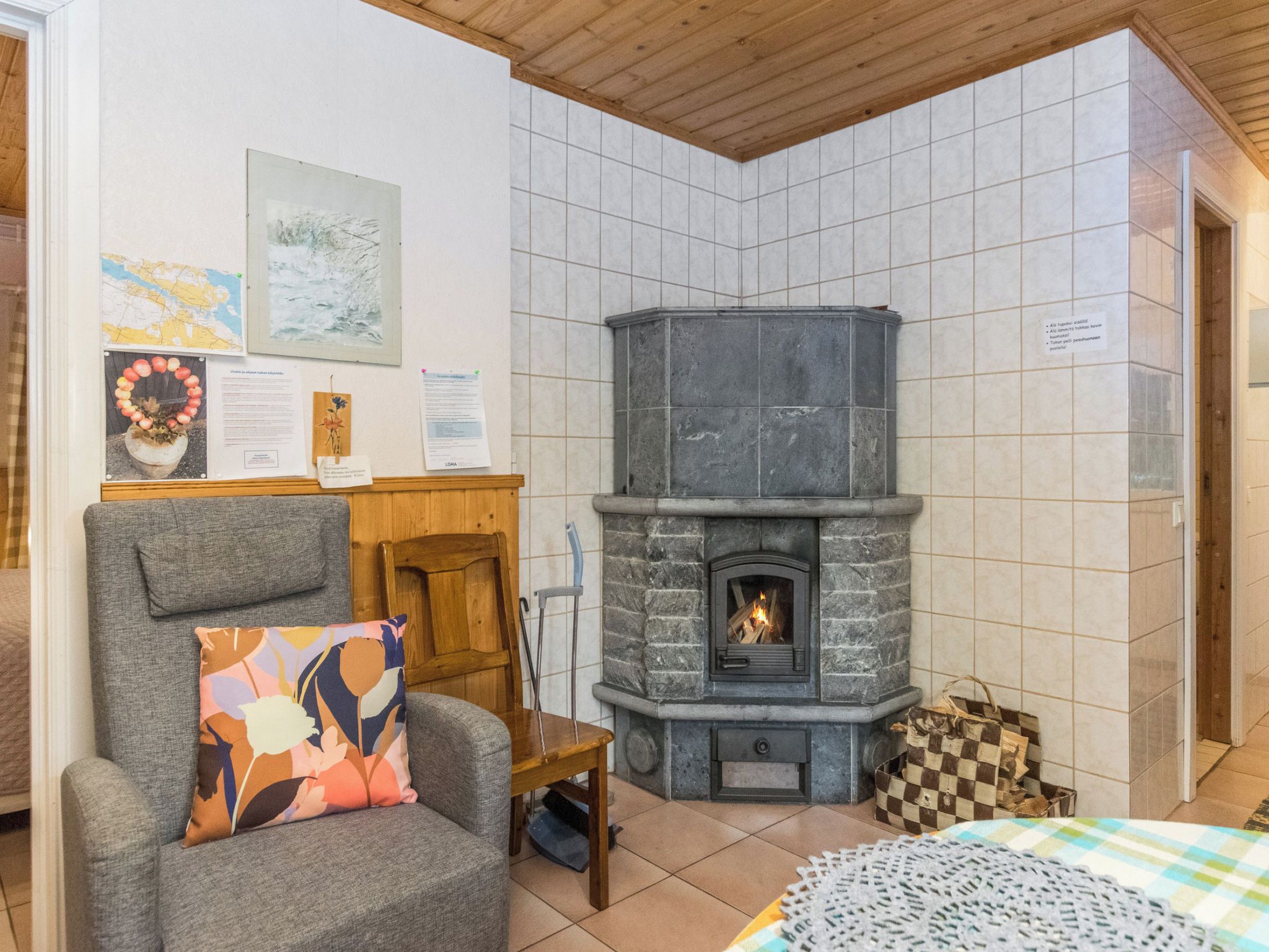 Ein gemütlicher Raum mit Kamin aus Stein, einem Holzstuhl mit farbigem Kissen und einem kleinen Tisch mit kariertem Beutel.