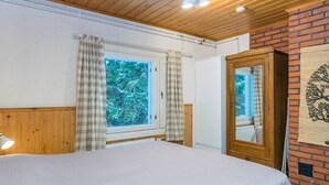 A bedroom with a large bed, wooden ceiling, a window with curtains, a mirror, and a brick wall with a tree design. - Mäkimökki by Interhome (Somero)