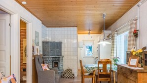 A cozy living room with a fireplace, a dining area with a table and chairs, and a kitchen with wooden cabinets. - Mäkimökki by Interhome (Somero)