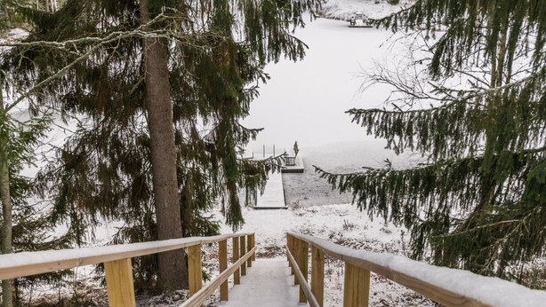 A wooden staircase leading to a dock over a snowy lake, surrounded by trees. - Mäkimökki by Interhome (Somero)