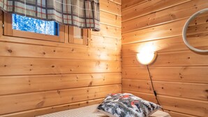 Ein Zimmer in einer Holzhütte mit einem Bett, einem Fenster mit Karottenvorhang und einer Wandleuchte.