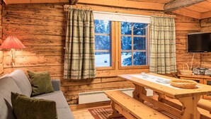 Ein gemütliches Blockhaus-Interieur mit Holzausstattung, einer Couch, einem Tisch und einem Fenster mit Vorhängen.