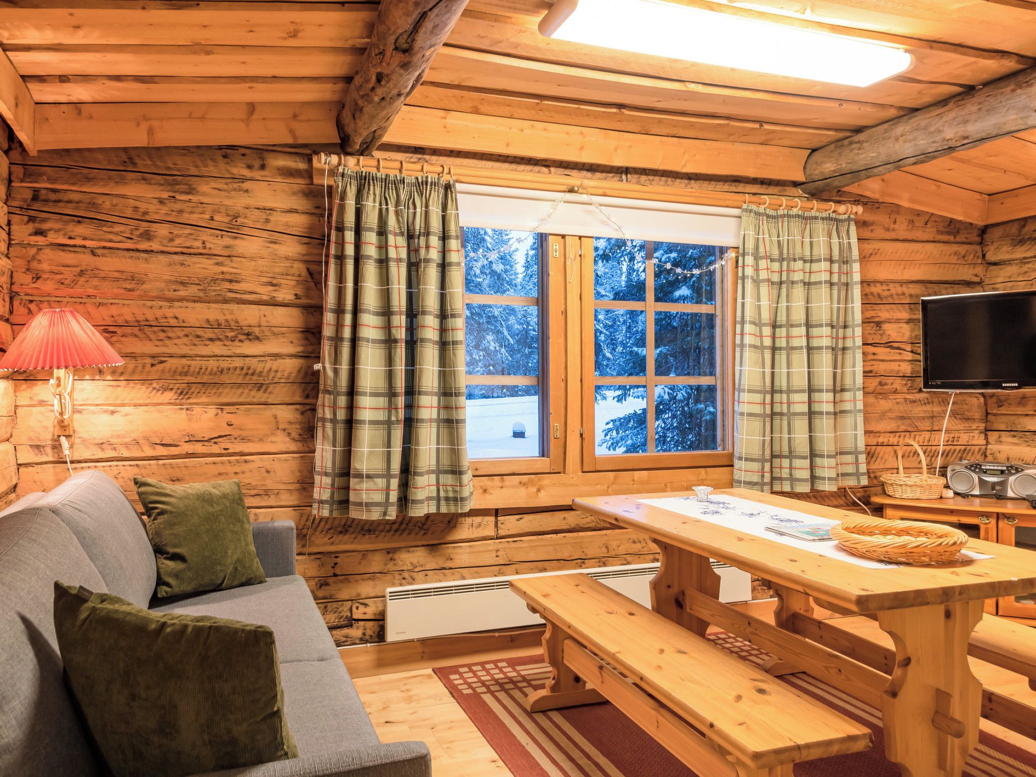 A cozy cabin interior with a wooden interior, a sofa, a table, and a window with curtains.
