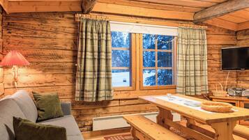 A cozy cabin interior with a wooden interior, a sofa, a table, and a window with curtains.