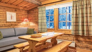 Ein gemütliches Blockhaus-Interieur mit einem Holztisch und Bänken, einer Couch, einer Lampe und einem Fenster mit Karottenvorhängen.