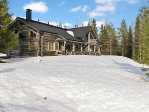 A log cabin with a large porch and a chimney, surrounded by snow and trees. - Peikkola by Interhome (Kuusamo)