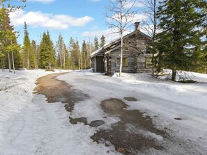 En hytte af tømmer med snedækket jord og en klar himmel.