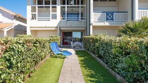 Un bâtiment à deux étages doté d’un balcon, d’un petit patio avec des chaises et d’une pelouse bien entretenue.