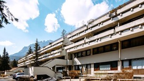 A multi-story hotel with balconies, a parking area, and a mountainous backdrop. - Solaria by Interhome (Canazei)