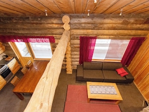 Ein gemütliches Blockhaus-Interieur mit Essbereich, Sofa und einer großen Holzbalkenkonstruktion.