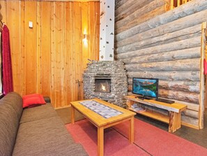 Ein rustikales Holzhaus-Interieur mit Kamin aus Stein, einer Couch, einem Couchtisch und einem Fernseher auf einem Holzboden.