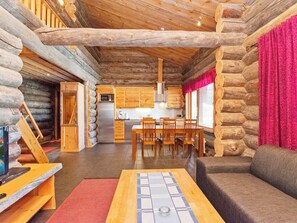 Interior de una cabaña de troncos con comedor, cocina y chimenea.