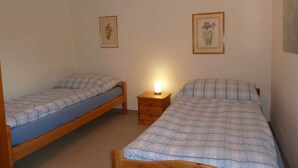 Une petite chambre propre, avec deux lits simples, une table de chevet et deux tableaux encadrés accrochés aux murs.