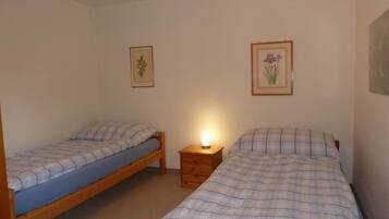 Ein kleines, sauberes Zimmer mit zwei Einzelbetten, einem Nachttisch und zwei gerahmten Bildern an den Wänden.