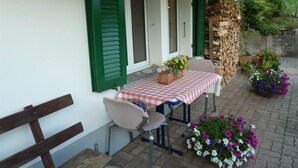 Un espace extérieur aménagé avec une table recouverte d’une nappe à carreaux, deux chaises et un banc.