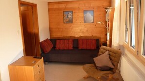 Une pièce chaleureuse avec un mur en bois, un canapé avec des coussins rouges, un meuble en bois et un radiateur.