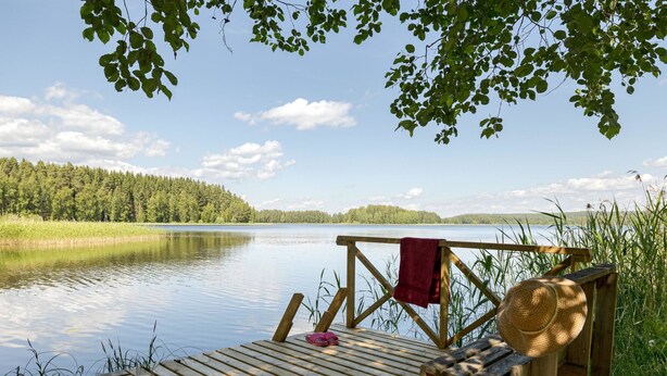 A wooden deck with a bench and a red towel, overlooking a calm lake with trees in the background. - Rinnekämppä by Interhome (Asikkala)