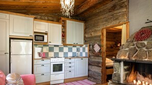 A cozy log cabin interior with a kitchen featuring white cabinets, a microwave, stove, and a stone fireplace with lit candles. - Rinnekämppä by Interhome (Asikkala)