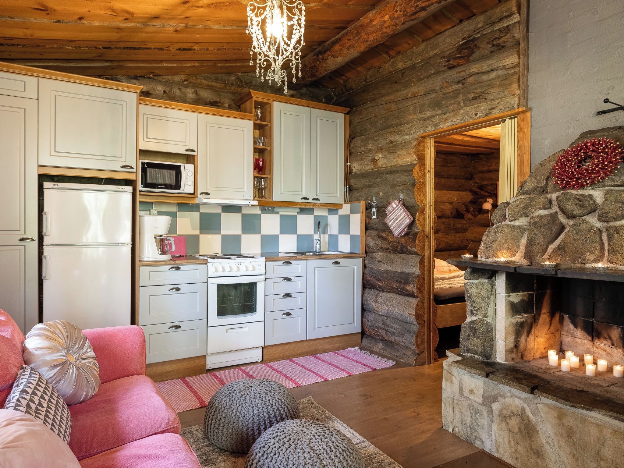 A cozy log cabin interior with a kitchen, a fireplace, and a living area with a sofa and cushions.
