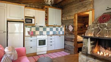 A cozy log cabin interior with a kitchen, a fireplace, and a living area with a sofa and cushions.