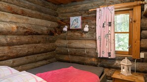 A cozy log cabin bedroom with a bed, a nightstand with a lantern, and a window with curtains. - Rinnekämppä by Interhome (Asikkala)