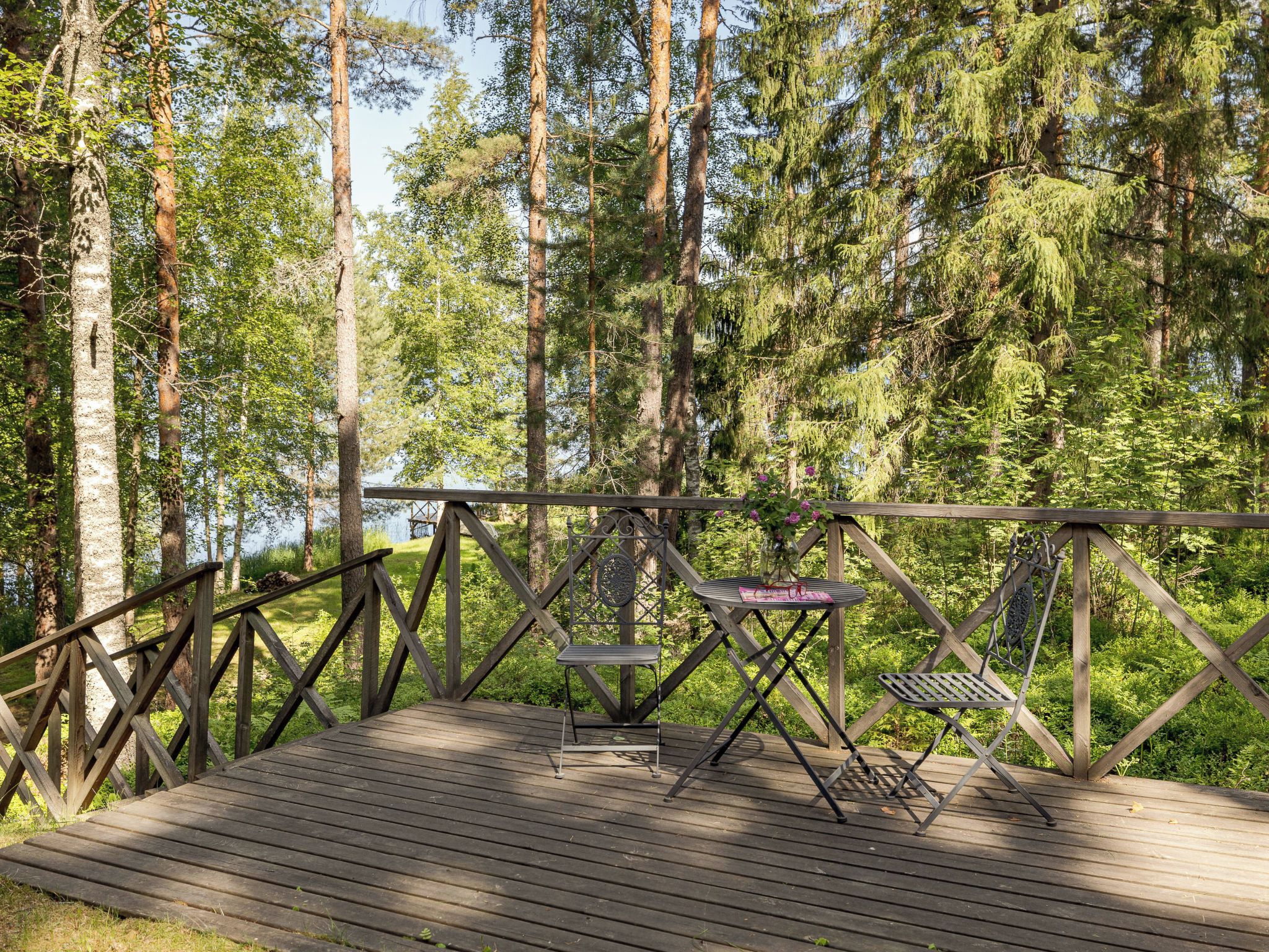 A wooden deck with metal chairs and a table, surrounded by tall trees.