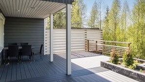 A covered outdoor area with a wooden deck, a seating arrangement, and a view of trees.