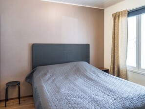 Une chambre à coucher avec un lit, une table de chevet, une chaise et une fenêtre avec des rideaux.